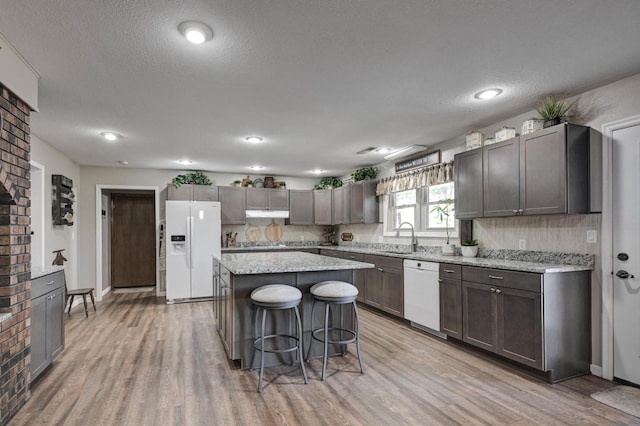 kitchen featuring a center island, white appliances, sink, light wood-type flooring, and a breakfast bar area