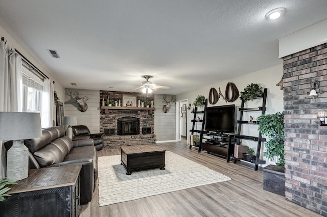 living room featuring ceiling fan, a brick fireplace, light hardwood / wood-style flooring, a textured ceiling, and wooden walls