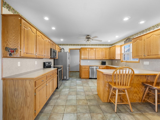 kitchen featuring ceiling fan, sink, kitchen peninsula, a breakfast bar area, and appliances with stainless steel finishes