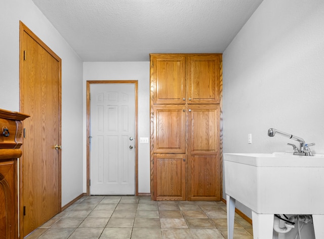 clothes washing area with light tile patterned flooring, sink, and a textured ceiling