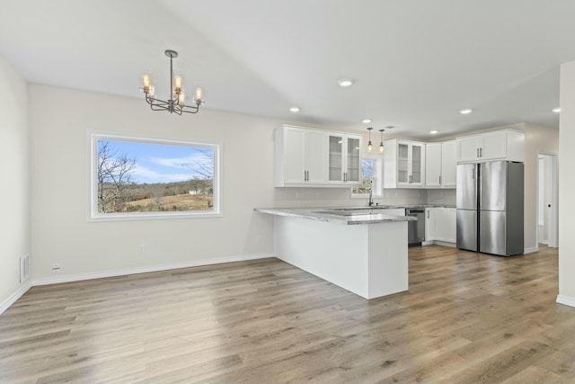 kitchen featuring kitchen peninsula, white cabinetry, stainless steel appliances, and decorative light fixtures