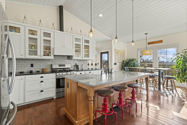 kitchen with stainless steel appliances, high vaulted ceiling, dark hardwood / wood-style floors, an island with sink, and dark stone counters