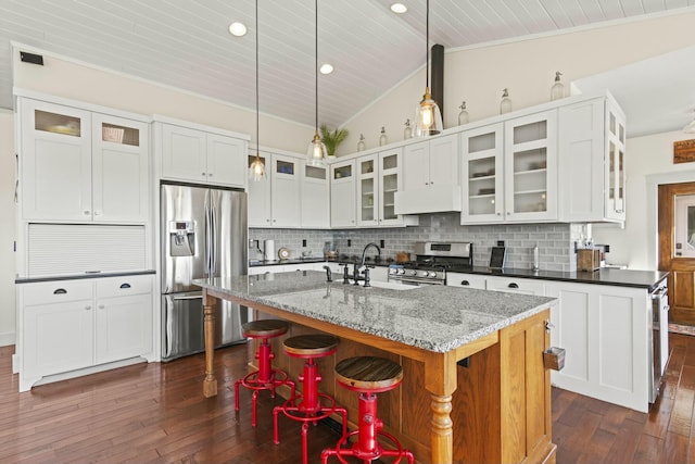 kitchen with dark stone counters, pendant lighting, an island with sink, and stainless steel appliances