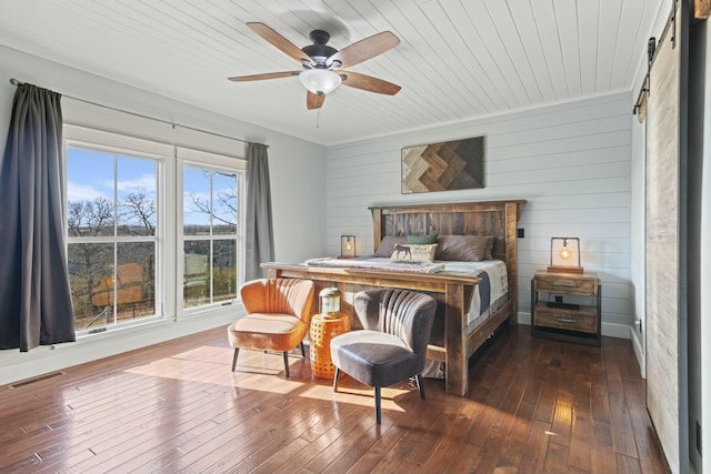 bedroom with wood walls, wooden ceiling, dark hardwood / wood-style floors, a barn door, and ceiling fan