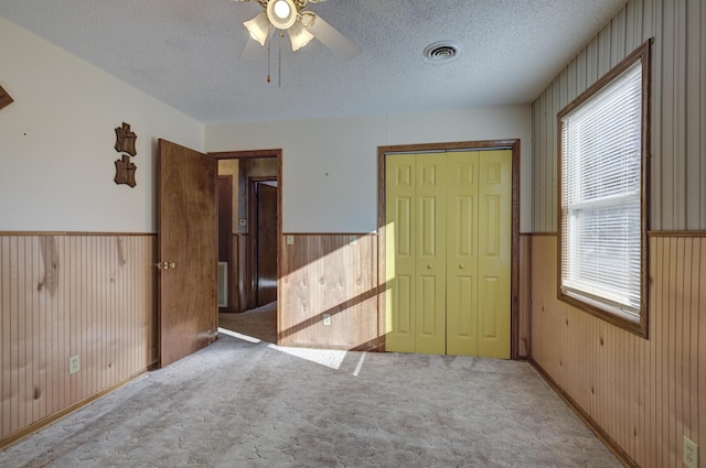 unfurnished bedroom with light carpet, wooden walls, ceiling fan, a textured ceiling, and a closet