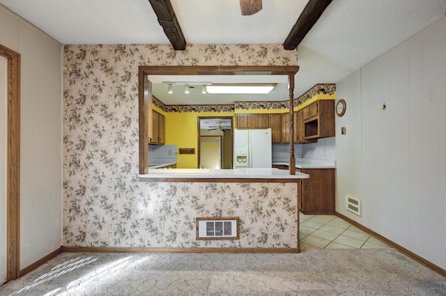 kitchen with a textured ceiling, kitchen peninsula, beamed ceiling, and white refrigerator with ice dispenser