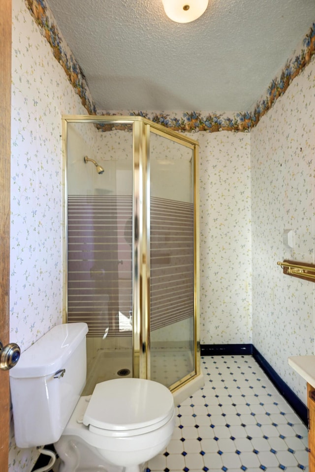 bathroom featuring a textured ceiling, toilet, and a shower with shower door