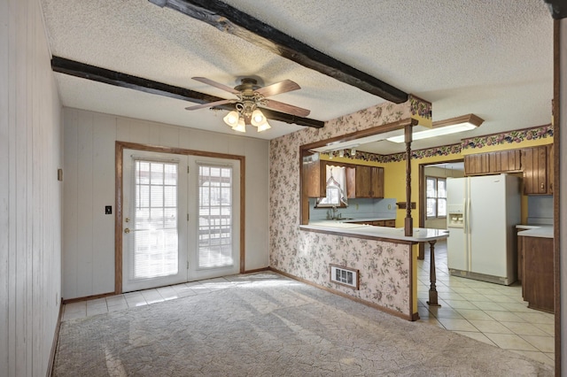 kitchen with ceiling fan, white fridge with ice dispenser, beamed ceiling, light tile patterned flooring, and kitchen peninsula