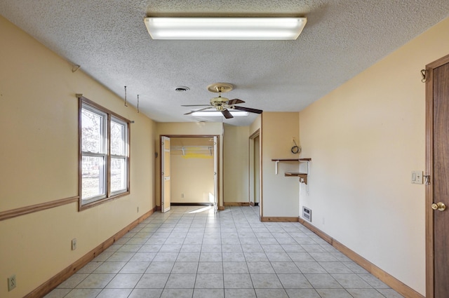 empty room featuring ceiling fan, light tile patterned floors, and a textured ceiling