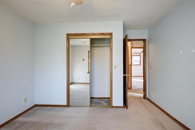 unfurnished bedroom with a textured ceiling, light colored carpet, a closet, and ceiling fan