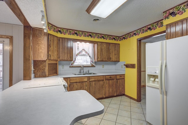 kitchen with kitchen peninsula, a textured ceiling, white appliances, sink, and light tile patterned floors