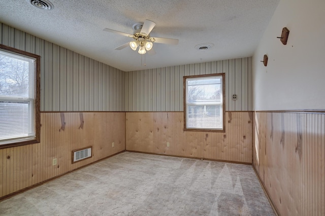 carpeted spare room with a textured ceiling, ceiling fan, and wooden walls