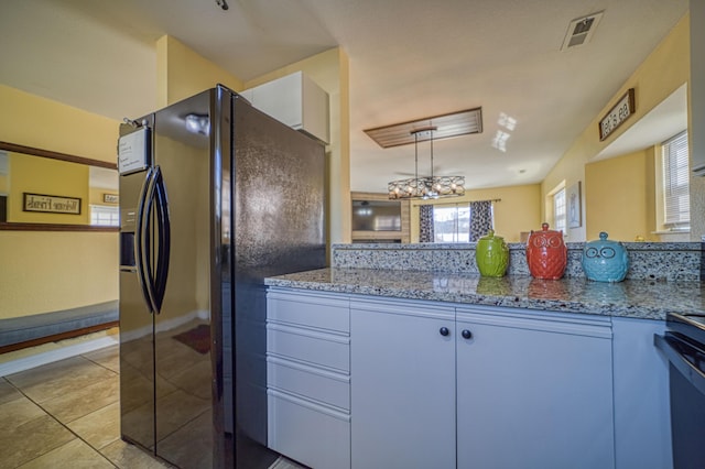 kitchen with light stone countertops, white cabinetry, hanging light fixtures, and black refrigerator with ice dispenser