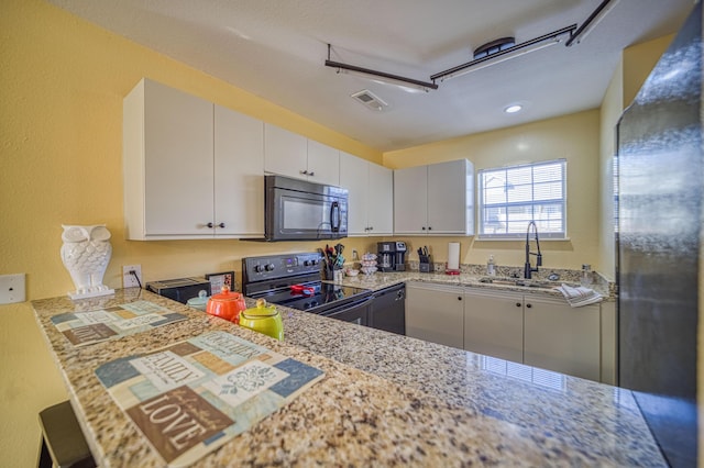 kitchen featuring black appliances, sink, white cabinetry, light stone counters, and kitchen peninsula