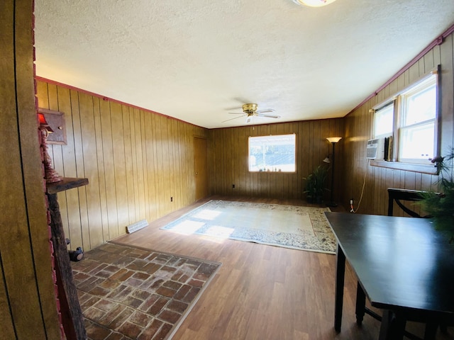 unfurnished living room featuring wood walls, ceiling fan, a healthy amount of sunlight, and dark wood-type flooring