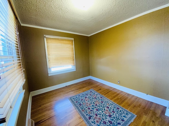 empty room with wood-type flooring, a textured ceiling, and ornamental molding