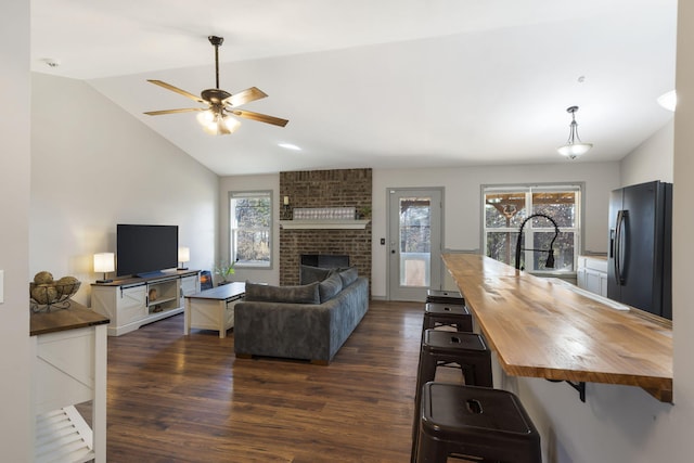 living room with a fireplace, plenty of natural light, dark wood-type flooring, and vaulted ceiling