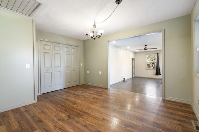 empty room with ceiling fan with notable chandelier, dark wood-type flooring, and a textured ceiling