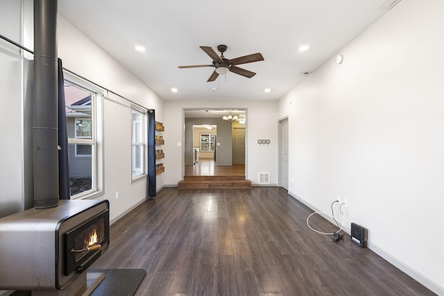 unfurnished living room with ceiling fan with notable chandelier, dark hardwood / wood-style flooring, and a wood stove