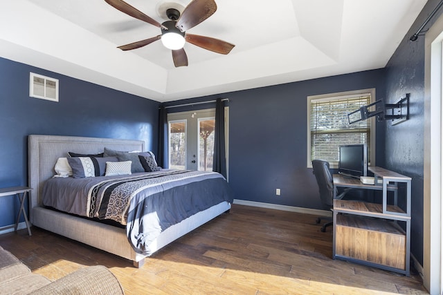 bedroom featuring a tray ceiling, multiple windows, ceiling fan, and wood-type flooring