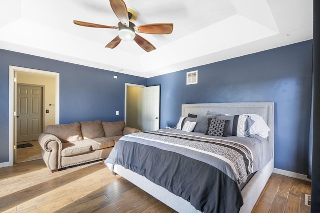 bedroom featuring ceiling fan, wood-type flooring, and a tray ceiling