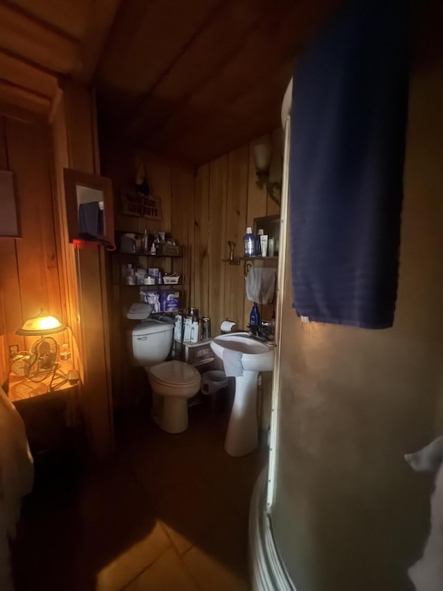 bathroom featuring tile patterned flooring, toilet, walk in shower, and wooden walls