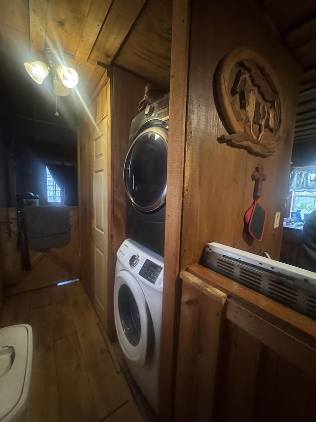 laundry area with wood-type flooring, stacked washer / dryer, and wood walls