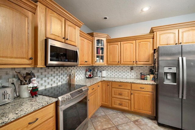 kitchen with tasteful backsplash, light stone counters, a textured ceiling, light tile patterned flooring, and appliances with stainless steel finishes