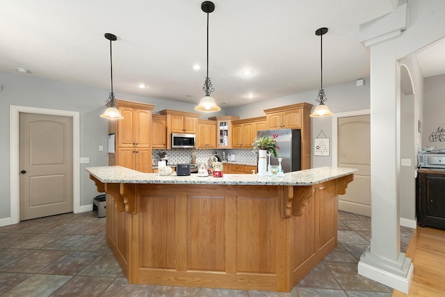 kitchen with backsplash, appliances with stainless steel finishes, decorative light fixtures, a kitchen island, and a breakfast bar area