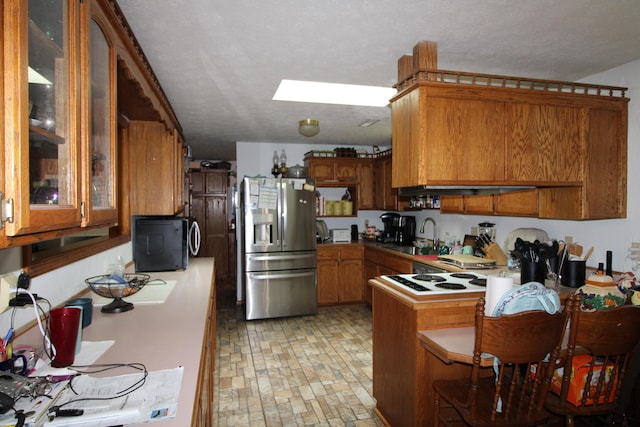 kitchen featuring a skylight, sink, kitchen peninsula, stainless steel fridge, and a textured ceiling