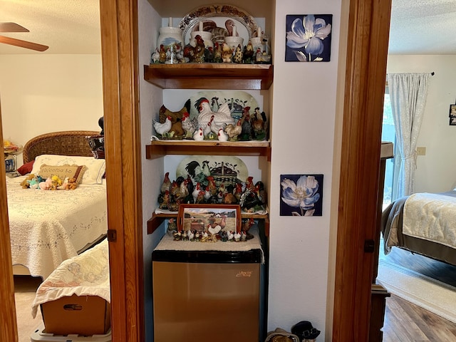 bedroom with ceiling fan, wood-type flooring, a textured ceiling, and fridge