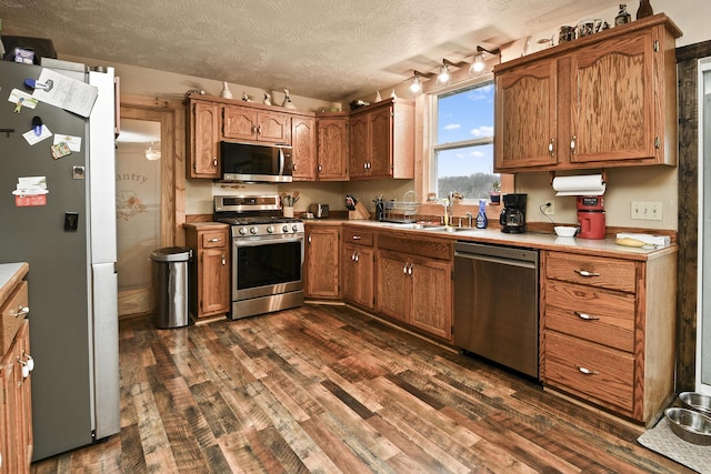 kitchen with track lighting, sink, dark hardwood / wood-style floors, a textured ceiling, and appliances with stainless steel finishes