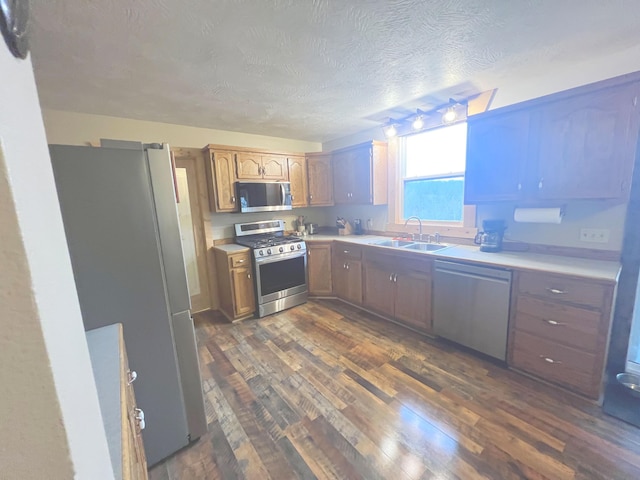 kitchen with a textured ceiling, sink, appliances with stainless steel finishes, and dark wood-type flooring