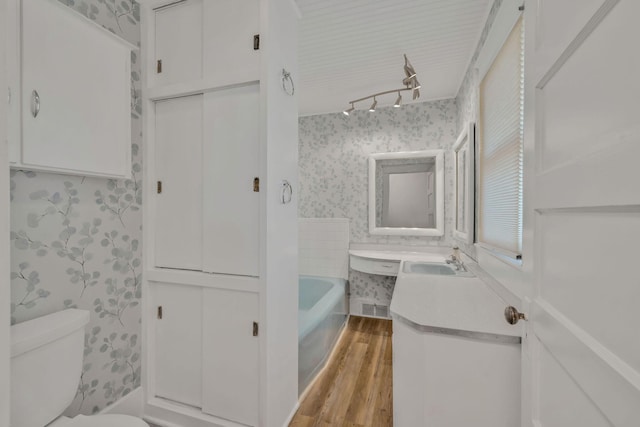 213 Mill St, Anderson, MO 64831 - bathroom with wallpapered walls, vanity, toilet, wood finished floors, and a tub to relax in
