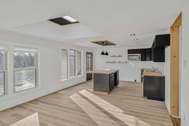 213 Mill St, Anderson, MO 64831 - kitchen featuring stainless steel microwave, dark cabinetry, a sink, light wood-style floors, and hanging light fixtures