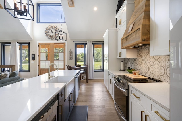 kitchen with white cabinets, appliances with stainless steel finishes, decorative light fixtures, and custom range hood