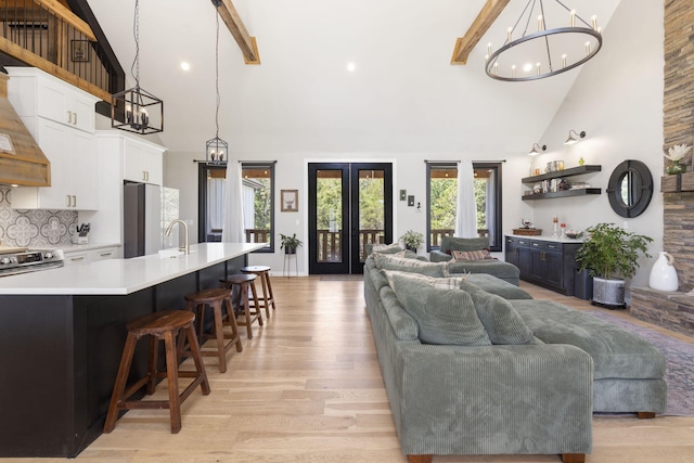 living room featuring high vaulted ceiling, french doors, sink, light hardwood / wood-style flooring, and beam ceiling