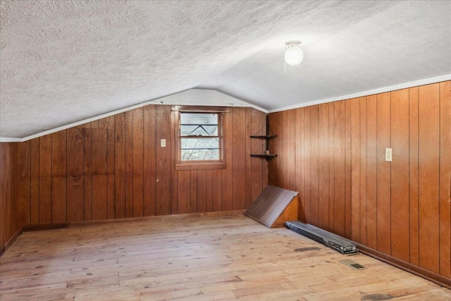 additional living space with vaulted ceiling, wooden walls, a textured ceiling, and light wood-type flooring