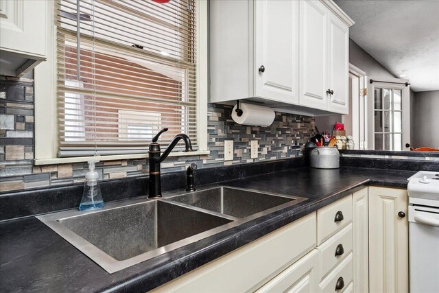 kitchen with a wealth of natural light, white electric range, sink, white cabinets, and backsplash