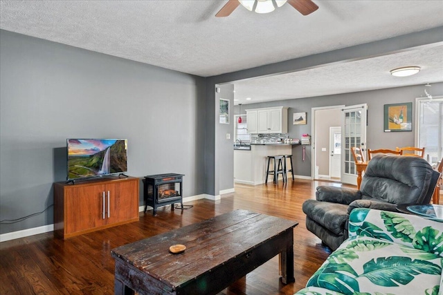 living room with ceiling fan, dark hardwood / wood-style flooring, a textured ceiling, and a wood stove