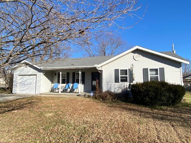 single story home with covered porch, a garage, and a front lawn