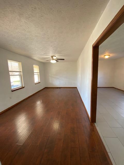 empty room with a textured ceiling, ceiling fan, and dark wood-type flooring