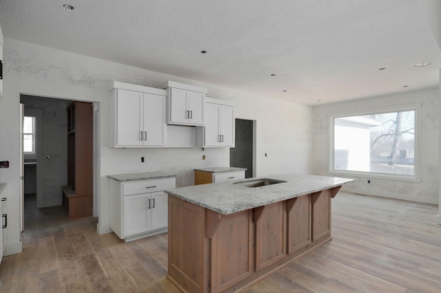 kitchen featuring white cabinetry, a healthy amount of sunlight, light hardwood / wood-style floors, and an island with sink