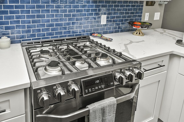 room details with white cabinets, light stone counters, stainless steel range with gas cooktop, and tasteful backsplash