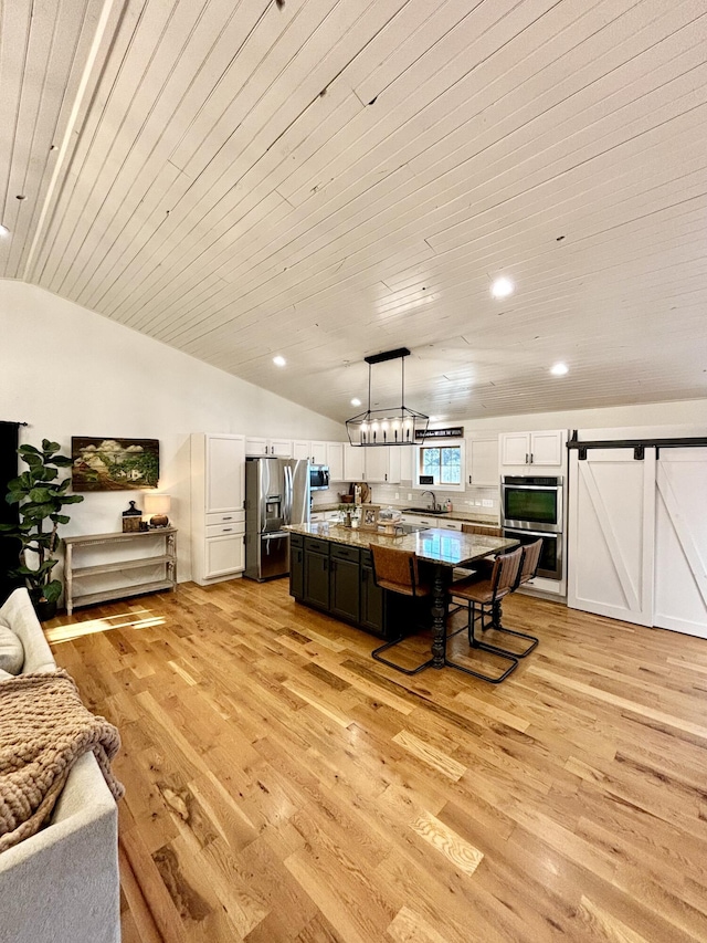 kitchen featuring a barn door, vaulted ceiling, decorative light fixtures, appliances with stainless steel finishes, and light wood-type flooring