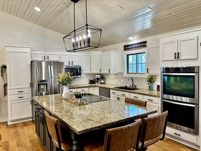 kitchen with light wood-type flooring, a kitchen island, backsplash, white cabinetry, and stainless steel appliances