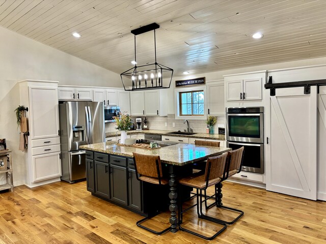 kitchen featuring a sink, appliances with stainless steel finishes, a barn door, backsplash, and a center island