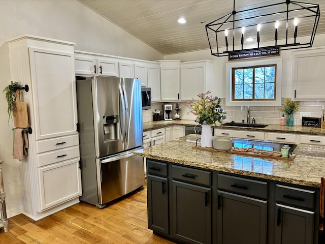 kitchen featuring a sink, vaulted ceiling, light wood-style floors, appliances with stainless steel finishes, and white cabinetry