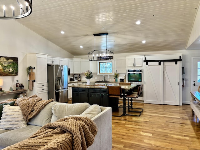 kitchen featuring white cabinets, appliances with stainless steel finishes, a barn door, a notable chandelier, and open floor plan