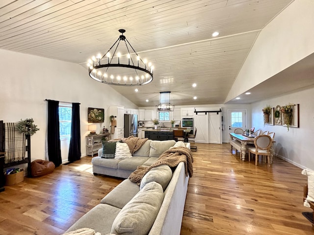 living area featuring light wood finished floors, a chandelier, high vaulted ceiling, and a barn door